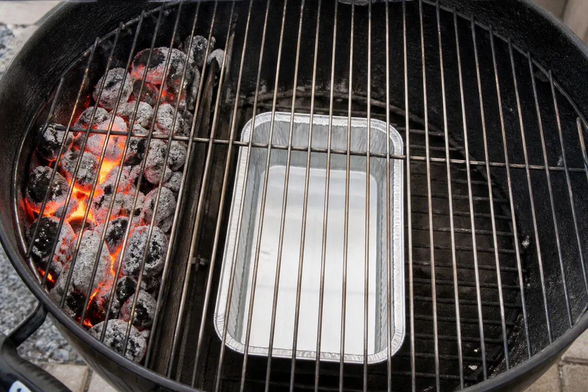 Braises rassemblées sur un côté de la cuve d’un barbecue à charbon, centre de la grille laissé libre
